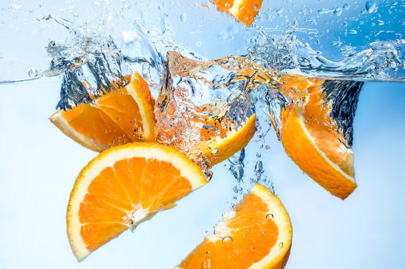 Orange fruits fall deeply under water with a big splash